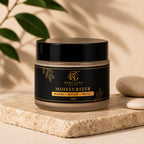 A jar of Rahi Luxa Organic Moisturizer sits on a textured stone slab with decorative leaves and smooth stones in the background. The product features a black label with gold lettering and botanical illustrations, topped with a black lid.